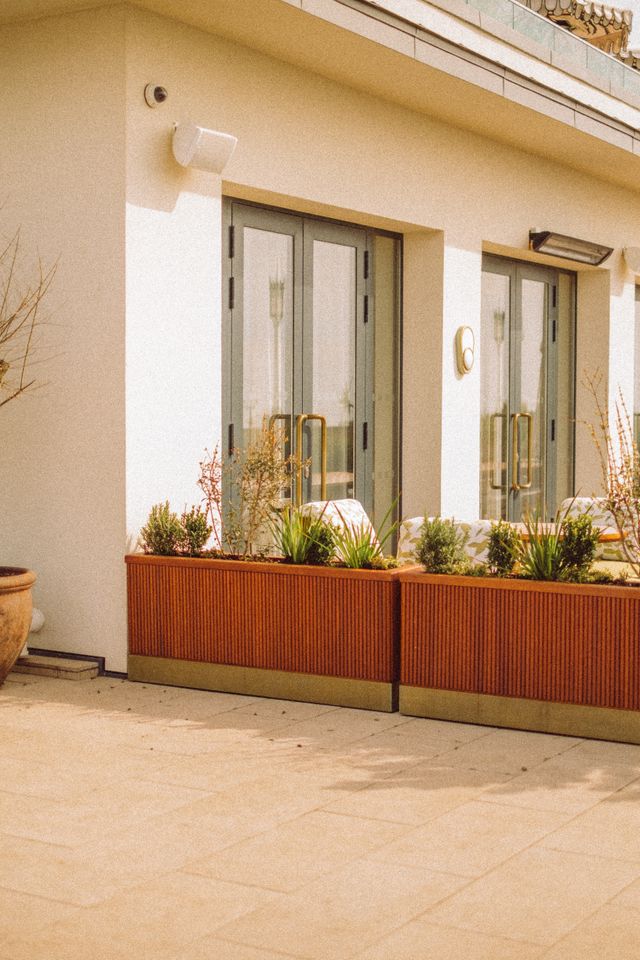 Mehrere Pflanzgefäße mit grünen Pflanzen stehen auf einer modernen Terrasse vor großen Glastüren.