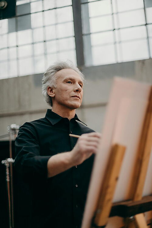 Technik & Ruhe am Arbeitsplatz Älterer Mann zeichnet konzentriert auf einem weißen Karton am Tisch – Symbolbild für sauberes, schrittweises Arbeiten und Technik beim Malen nach Zahlen.