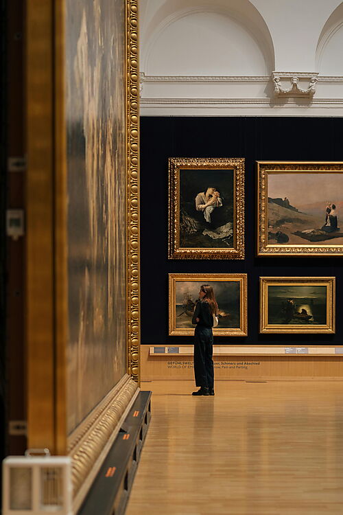 Eine Person betrachtet in einer Galerie mehrere großformatige Gemälde.