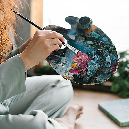 Person malt zu Hause mit einem Pinsel an einem Kunstprojekt – Symbolbild für Malen nach Zahlen als alltagstaugliches Ritual und kreative Routine.