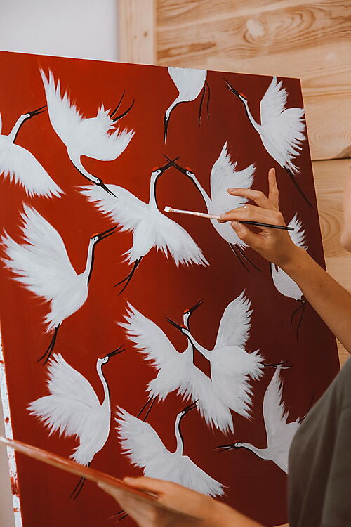 Frau malt ein Vogelmotiv auf einer Leinwand – Symbolbild für unterschiedliche Schwierigkeitsgrade beim Malen nach Zahlen.