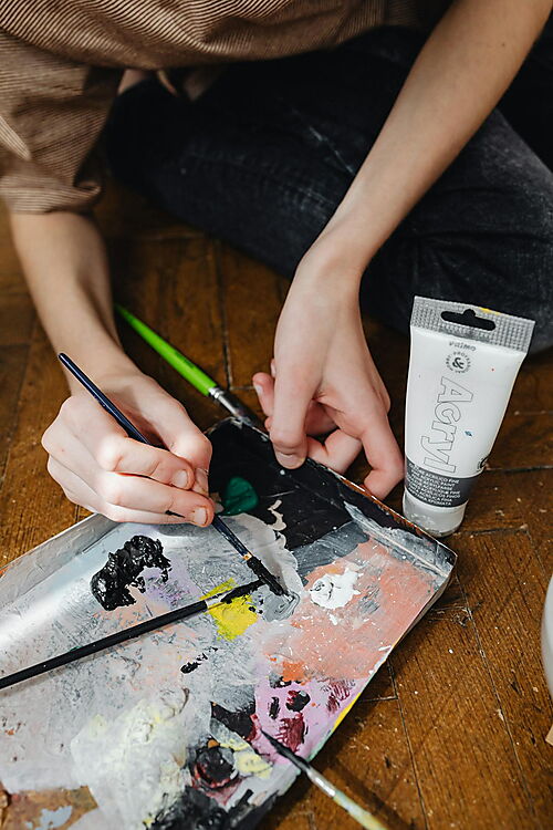 Hände arbeiten mit Pinsel und Acrylfarben auf einer Mischpalette und zeigen den praktischen Einstieg in Technik und erste Übungen.