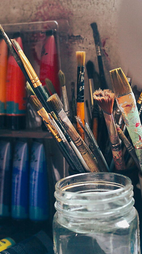 Acrylmalerei für Anfänger – Material und Arbeitsplatz Pinsel, Acrylfarben und Malzubehör auf einem kreativen Arbeitsplatz als Einstieg in Material und Setup der Acrylmalerei.