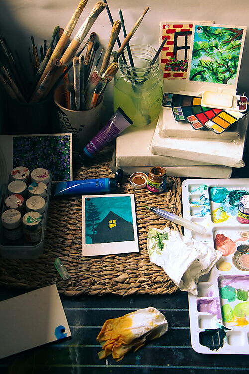 Kreativer Arbeitsplatz mit Pinseln, Farbpalette, Farbdosen und Ateliermaterialien als Inspiration für den Einstieg in die Acrylmalerei.