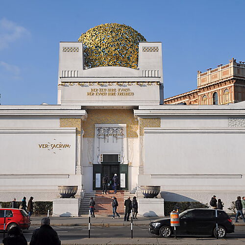 Frontansicht des weißen Gebäudes der Wiener Secession mit symmetrischer Fassade, vergoldeter Lorbeerkuppel und dem Wahlspruch über dem Eingang.