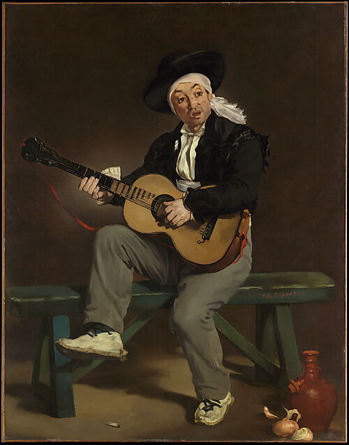 Ein sitzender Mann in spanisch anmutender Kleidung spielt Gitarre vor einem dunklen Hintergrund.