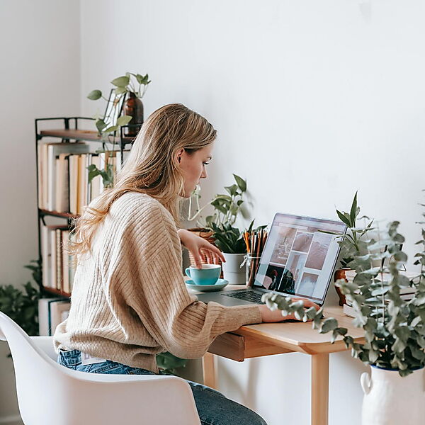 Frau sitzt am Schreibtisch mit Laptop und Kaffee und recherchiert online – Symbolbild für Preisvergleich und Auswahl eines Malen-nach-Zahlen-Sets im Internet.