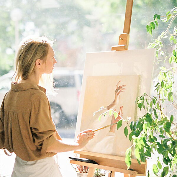 Frau steht nachdenklich neben einer grünen Zimmerpflanze – Symbolbild für Pause, Selbstfreundlichkeit und Neustart, wenn die Motivation beim Malen nach Zahlen fehlt.