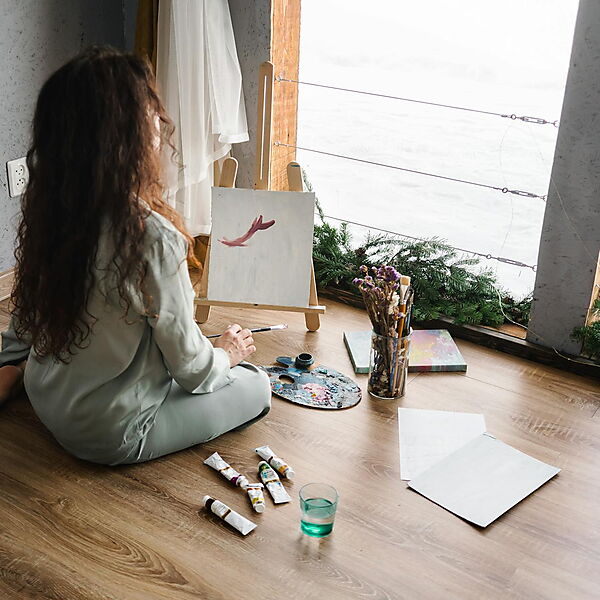 Person sitzt drinnen auf dem Boden und malt konzentriert an einer Leinwand – Symbolbild für Flow, Ruhe und kleine kreative Auszeiten mit Malen nach Zahlen.