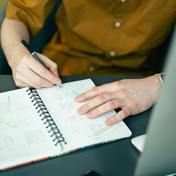 Hand zeichnet und entwickelt Ideen in einem Notizbuch an einem kreativen Schreibtisch.