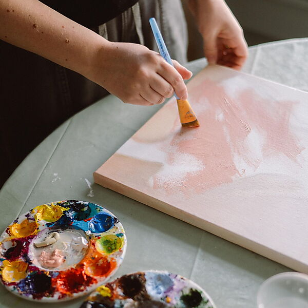 Person malt mit Acrylfarben ein abstraktes Bild auf Leinwand und arbeitet frei mit Formen, Flächen und Farben.