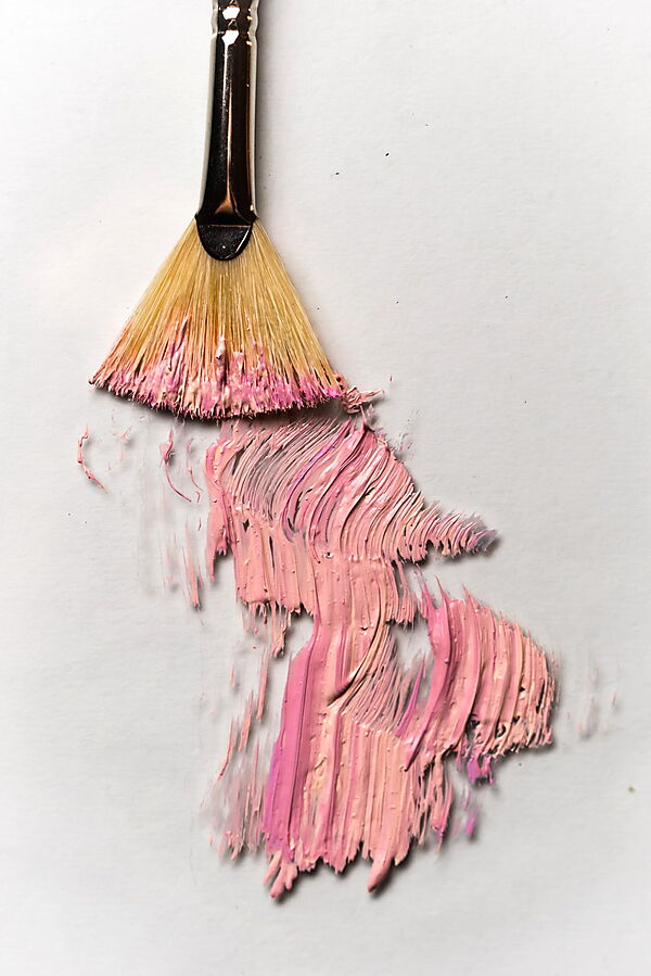 Ein Pinsel zieht rosa Acrylfarbe in sichtbaren Spuren über eine helle Leinwand