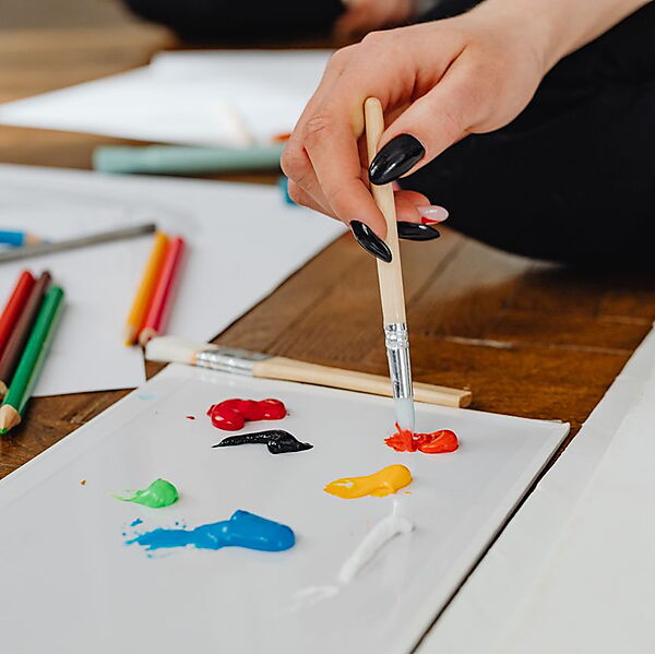 Eine Hand führt einen Pinsel über eine kleine Farbfläche auf Papier