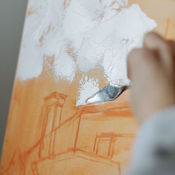Eine helle Acrylschicht wird über eine orangefarbene Untermalung auf der Leinwand aufgetragen
