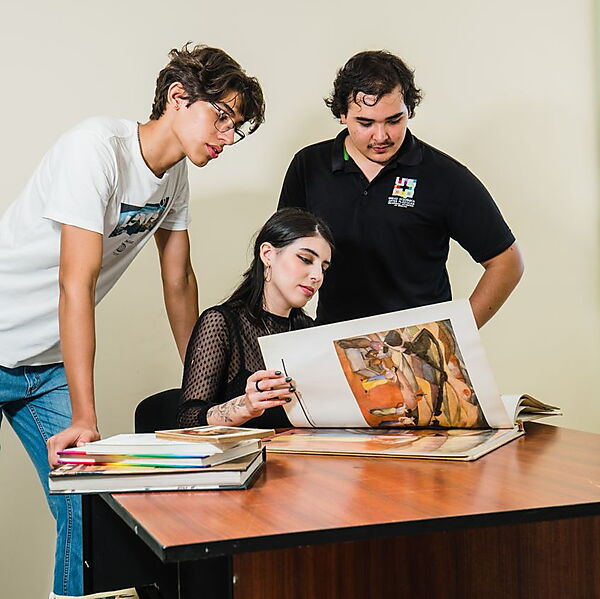 Studierende betrachten gemeinsam Abbildungen von Kunstwerken in aufgeschlagenen Büchern und tauschen ihre Beobachtungen aus.