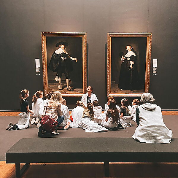 Eine Lehrerin bespricht mit einer Gruppe von Kindern mehrere Gemälde in einem Kunstmuseum.