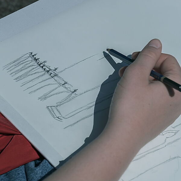 Hand zeichnet mit einem Bleistift die ersten einfachen Linien eines Gebäudes auf weißes Papier