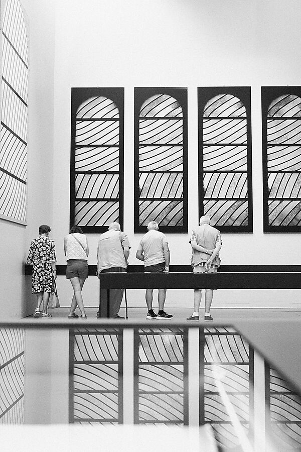 Museumsbesucher und Kunstwerke überlagern sich in den spiegelnden Flächen eines modernen Ausstellungsraums