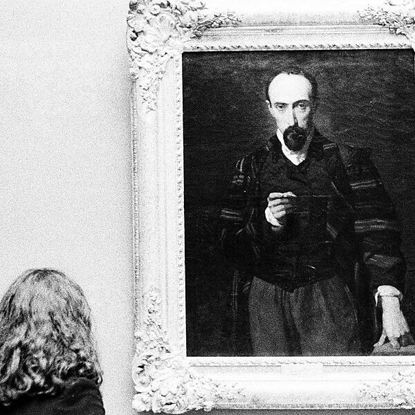 Frau betrachtet ein gerahmtes Porträt in einem Museum und achtet auf Blick, Mimik und Gesichtsausdruck der dargestellten Figur.