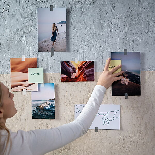 Frau ordnet verschiedene Fotografien und eine Linienzeichnung an einer Inspirationswand.