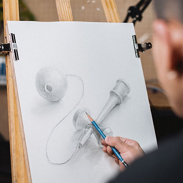 Ein Zeichner skizziert ein Kendama und baut das Motiv sichtbar aus Kugel, Zylinder und geschwungenen Linien auf.