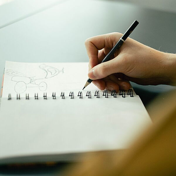 Hand zeichnet mit Bleistift abstrakte Linien in ein Skizzenbuch und zeigt einen freien, suchenden Zeichenmoment.