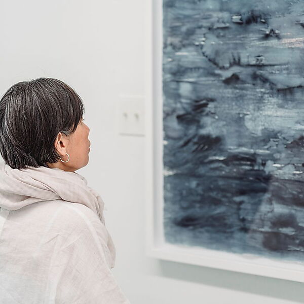 Frau betrachtet ein abstraktes Gemälde in einer modernen Galerie und nähert sich dem Bild aufmerksam und fragend.