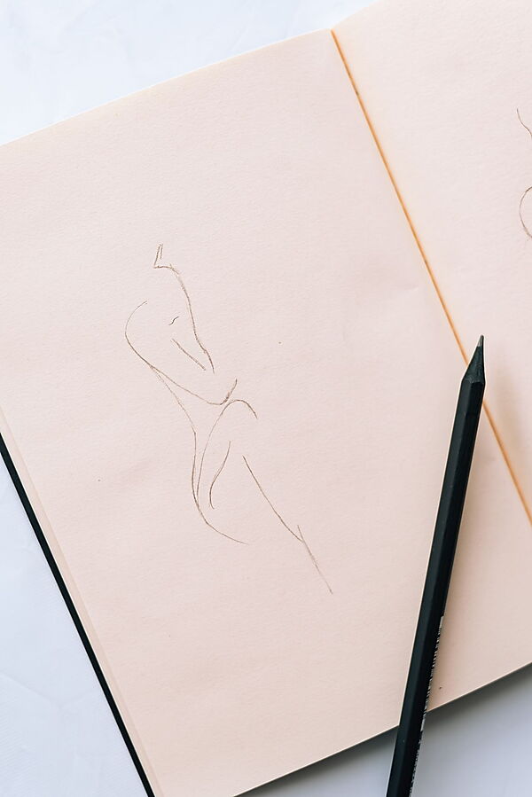 Hand skizziert mit einem Bleistift eine einfache Linienzeichnung in ein offenes Notizbuch.