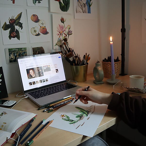 Kreativer Arbeitsplatz mit Laptop, Zeichenmaterial und floralen Skizzen zeigt, wie Online-Angebote beim Zeichnenlernen inspirieren können.