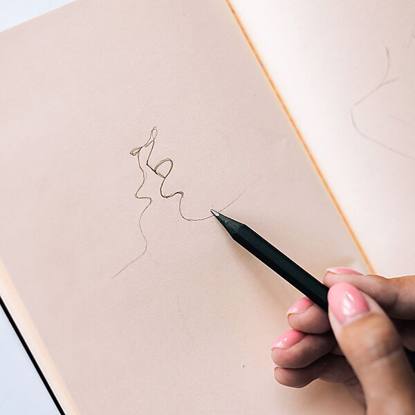 Hand zeichnet mit einem Bleistift erste lockere Linien in ein fast leeres Skizzenbuch.