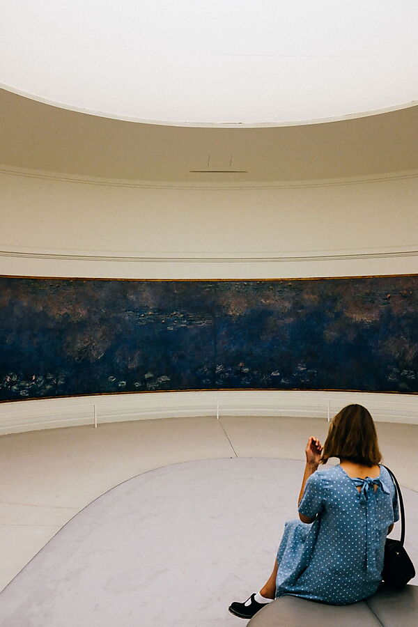 Frau im blauen Kleid, auf einem weichen Hocker sittzend, betrachtet allein die die Nymphéas von Claude Monet, mehrere großformatige Landschaftsbilder, im "Musée de l'Orangerie" in Paris.