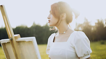 Frau steh im Sommer auf einer Wiese und malt – Symbolbild für Entspannung, Achtsamkeit und kreative Pause beim Malen nach Zahlen.