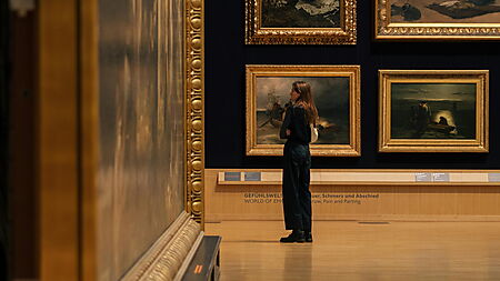 Eine Person betrachtet in einer Galerie mehrere großformatige Gemälde.