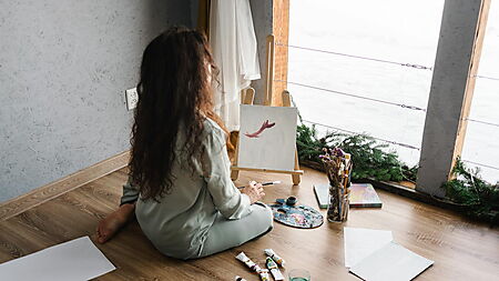 Person sitzt drinnen auf dem Boden und malt konzentriert an einer Leinwand – Symbolbild für Flow, Ruhe und kleine kreative Auszeiten mit Malen nach Zahlen.