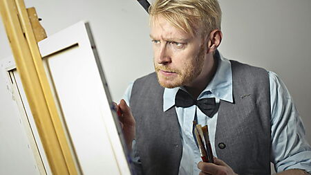 Konzentrierter Mann malt auf einer Leinwand im Studio – Symbolbild für geführtes Malen und kreative Praxis.