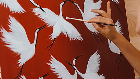 Frau malt ein Vogelmotiv auf einer Leinwand – Symbolbild für unterschiedliche Schwierigkeitsgrade beim Malen nach Zahlen.