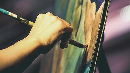 Person malt an einer Leinwand – Symbolbild für verschiedene DIY-Kunstformen und den Reiz kreativer Hobbys im Vergleich.