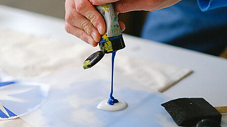 Hand arbeitet mit Pinsel und Acrylfarbe an einer Farbfläche und zeigt den praktischen Umgang mit Material und Farbauftrag.