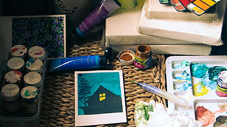 Kreativer Arbeitsplatz mit Pinseln, Farbpalette, Farbdosen und Ateliermaterialien als Inspiration für den Einstieg in die Acrylmalerei.