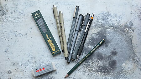 Zeichen- und Schreibwerkzeuge wie Bleistift, Fineliner und Zubehör liegen geordnet auf einem Schreibtisch.