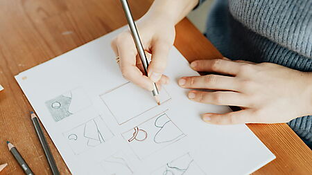 Frau zeichnet mit Bleistift auf Papier und übt erste Zeichentechniken an einem kreativen Arbeitsplatz.