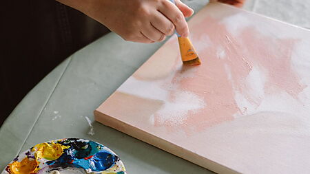 Person malt mit Acrylfarben ein abstraktes Bild auf Leinwand und arbeitet frei mit Formen, Flächen und Farben.