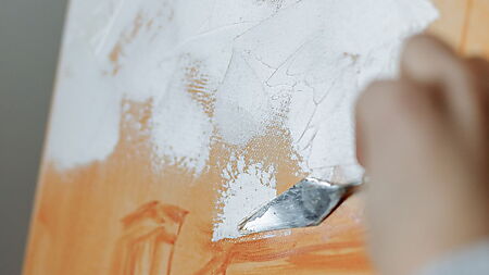 Eine helle Acrylschicht wird über eine orangefarbene Untermalung auf der Leinwand aufgetragen