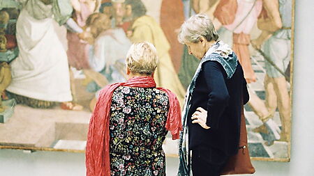 Zwei Frauen betrachten gemeinsam ein Gemälde in einer Galerie und tauschen sich über Wirkung und Bedeutung des Bildes aus.