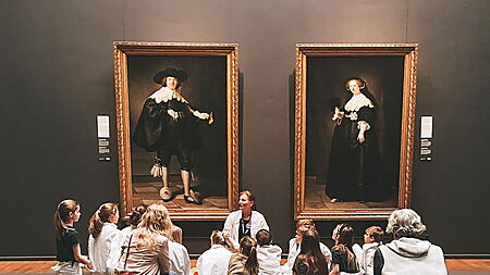 Eine Lehrerin bespricht mit einer Gruppe von Kindern mehrere Gemälde in einem Kunstmuseum.