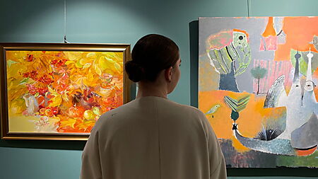 Eine Frau betrachtet farbige abstrakte Gemälde an einer blauen Galeriewand.