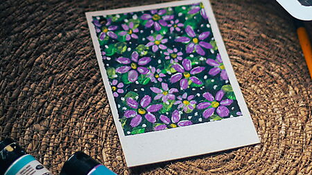 Ein einfaches florales Acrylmotiv liegt mit Pinseln und Farben auf einem Arbeitstisch