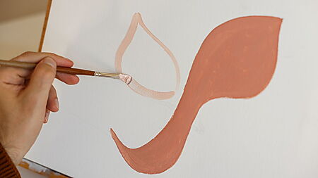 Hand malt mit einem Pinsel einfache abstrakte Formen auf eine Leinwand und plant so den Bildaufbau mit Acrylfarben.