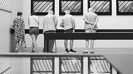 Museumsbesucher und Kunstwerke überlagern sich in den spiegelnden Flächen eines modernen Ausstellungsraums