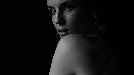 Schwarz-Weiß-Porträt einer Frau, die vor dunklem Hintergrund über ihre Schulter zurückblickt Bildtitel: Ein Blick zwischen Nähe und Geheimnis